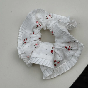 Détail d'un chouchou blanc avec motifs de fleurs rouges et bords en dentelle plissée