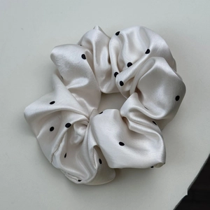 Gros plan détaillé d'un chouchou en satin crème avec pois noirs et texture soyeuse