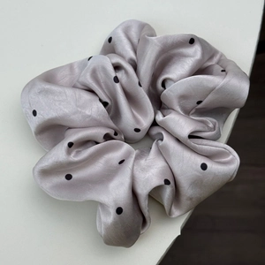 Gros plan sur un chouchou en satin gris clair avec motif classique à pois noirs