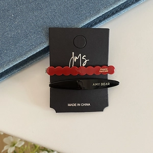 Detail of red wavy and black oval acetate hair clips with gold lettering on card