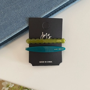 Detailed macro view of olive green wavy and dark teal oval acetate hair clips on card
