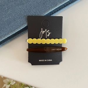 Close-up of wavy yellow acetate hair clip and tortoise shell barrette on display card