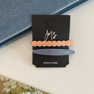 Detail of colorful acetate hair clips in orange and blue on a black display card