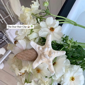 Barrette étoile de mer chic avec base tressée posée sur des fleurs blanches