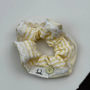 Détail du chouchou en tissu à rayures jaunes avec bordure en dentelle et bouton décoratif