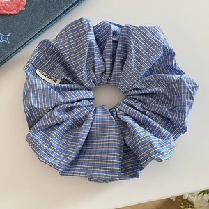Close-up of blue plaid scrunchie with logo tag on a clean white decorative background