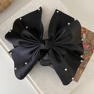 Détail d'une grande pince à cheveux en satin noir avec nœud orné de perles élégantes