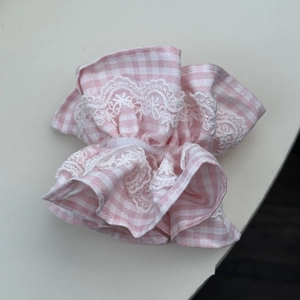 Gros plan d'un chouchou en tissu vichy rose avec bordure en dentelle blanche et froufrous