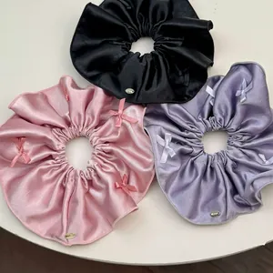 Three elegant satin bow scrunchies in black, pink and purple with metal logo tags