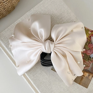 Détail d'une pince à cheveux en satin champagne avec nœud élégant et perles blanches