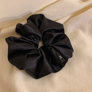 Détail d'un chouchou en satin noir avec un logo nœud blanc sur une étiquette en tissu noir