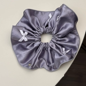 Detail of lilac satin scrunchie with white bows and a silver brand charm