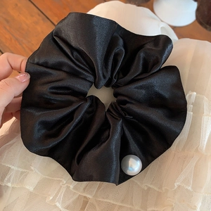 Close-up of black satin scrunchie featuring smooth fabric texture and pearl detail decoration
