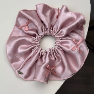 Close-up of pink satin scrunchie featuring delicate bows and a small gold metal tag