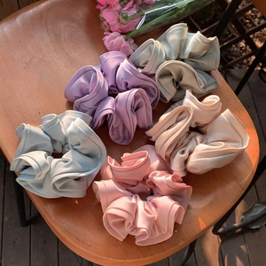 Cinq chouchous en satin de soie aux couleurs pastel sur une chaise en bois