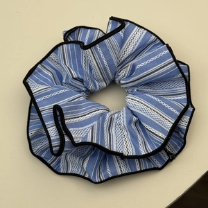 Close-up of blue and white striped fabric scrunchie with black ruffled edges and soft texture
