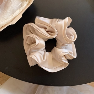 Vue détaillée du chouchou en satin champagne avec plis multicouches sur fond sombre