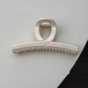 Detail of creamy white resin hair claw clip with golden metal spring and smooth finish