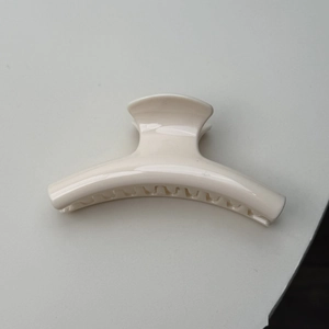 Detail view of the cream-colored minimalist hair claw clip with glossy finish