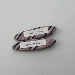 Detail van twee gestreepte stoffen haarspelden met Smile Life labels op grijze ondergrond