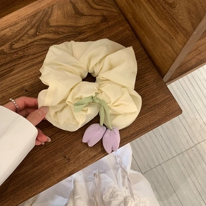 Detailed shot of cream tulip scrunchie with purple flower pendant on a wooden background
