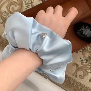 Detail of light blue satin scrunchie with white pearls and a silver heart buckle decoration