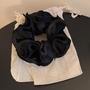 Large black satin ruffled hair scrunchie with layered fabric on a white linen drawstring pouch