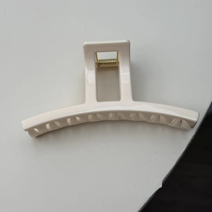 Close-up of minimalist off-white hair claw clip with golden spring and glossy finish