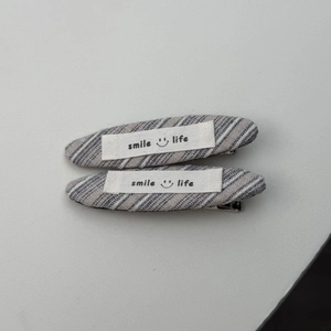 Detail van haarclips met grijs gestreepte twill stof en smile life stoffen label