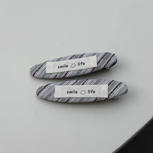 Detail van gestreepte stoffen haarclips met smile life borduursel en linnen textuur