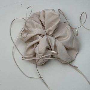 Detail shot of beige cotton scrunchie with delicate ribbon bows and soft fabric texture