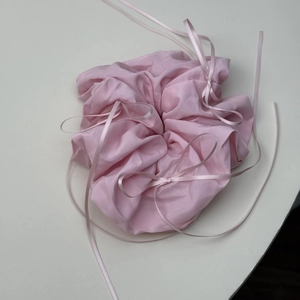 Close-up of light pink pleated scrunchie with delicate ribbon bows and shiny fabric