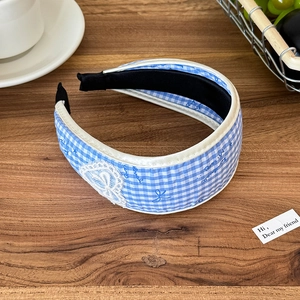Detail eines blau karierten Haarreifs mit weißer Spitzenschleife auf rustikalem Holztisch