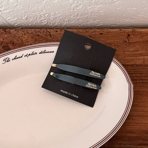 Deep green acetate hair clip set with gold lettering on a vintage white ceramic plate