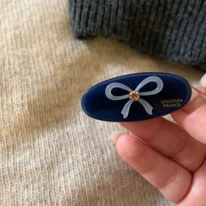 Dark blue oval hair clip with light blue bow and amber crystal detail in hand