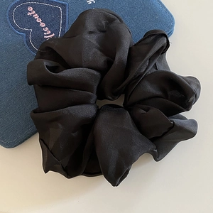Detailed close-up of a black satin scrunchie featuring elegant glossy folds and texture