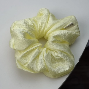 Macro shot of a light yellow textured silk scrunchie featuring a Hand Made woven label