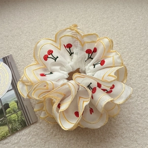 White embroidered cherry scrunchie with yellow scalloped edges on soft plush background