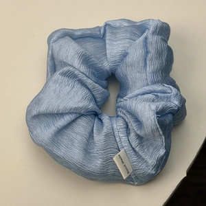 Detail of light blue wrinkled fabric scrunchie with a white Hand Made textile label