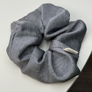 Close-up of dark grey pleated scrunchie with silk sheen and Hand Made textile label