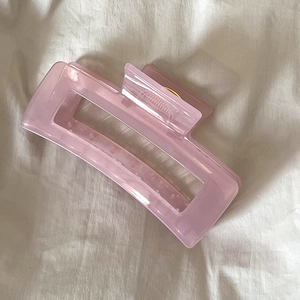 Détail de la pince à cheveux rose translucide avec ressort doré sur tissu