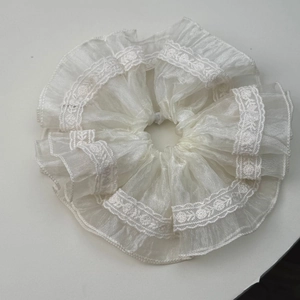 Detail of white ruffled lace scrunchie made of light organza fabric with intricate floral embroidery