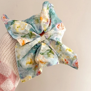 Close-up of a floral chiffon scrunchie in light blue with pink and yellow watercolor patterns
