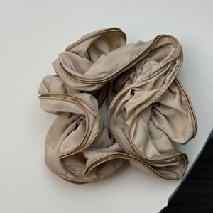 Close-up of champagne satin scrunchie featuring elegant ruffled edges and smooth texture
