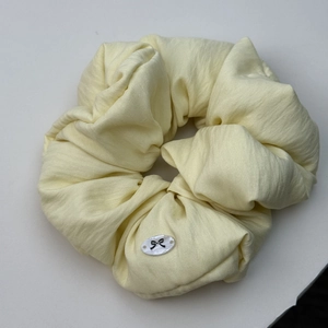 Nahaufnahme eines hellgelben Scrunchie-Haargummis mit kleinem schwarzen Schleifenanhänger