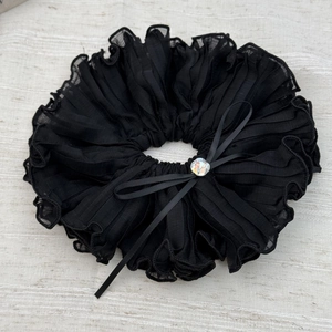 Dettaglio macro dello scrunchie plissettato nero con fiocco di cristallo e gemma iridescente