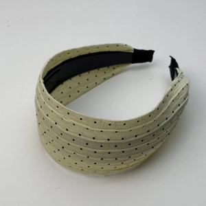 Detail eines cremegelben plissierten Stirnbands mit schwarzen Punkten und breitem Rand