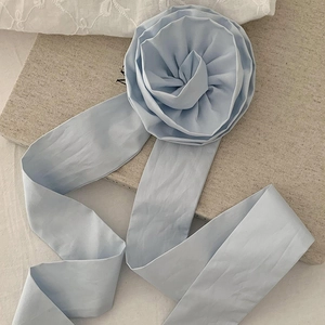 Détail d'un accessoire fleur en tissu bleu clair avec long ruban sur fond beige