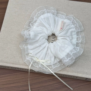 Scrunchie in pizzo bianco con fiocco di nastro ed etichetta fatta a mano su libro