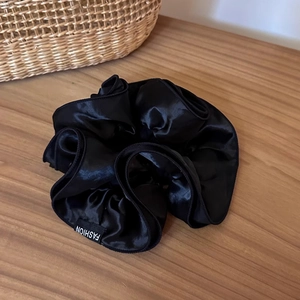 Detailed close-up of a large black satin scrunchie with a Fashion woven label